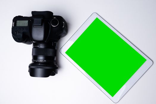 Top view of a black digital camera and a blank screen tablet on a table.