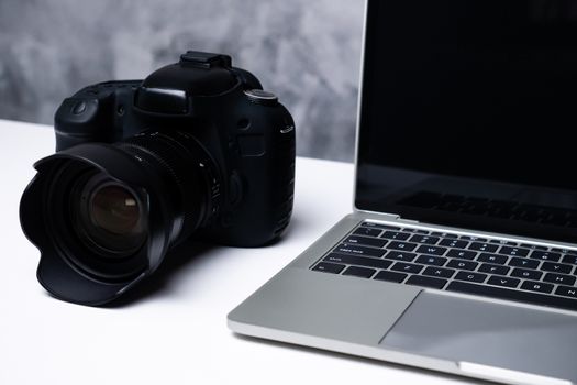 A black digital camera and a computer laptop on a table.