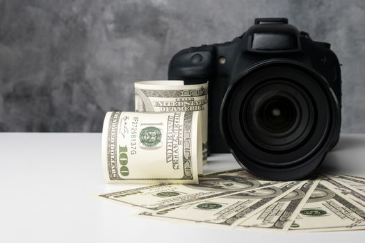 A black digital camera and banknotes on a white table with grunge background.