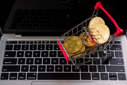 Golden coins with bitcoin symbol in a little shopping cart on a computer keyboard.