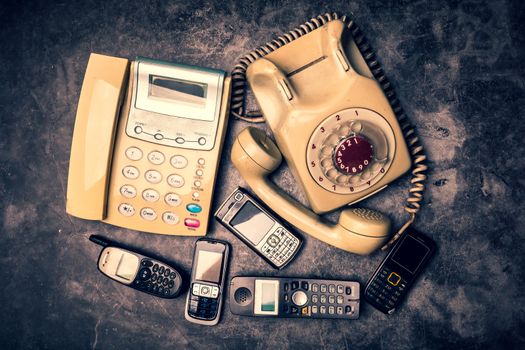 An old telephone with rotary dial, landline and obsoleted cellphone on a grunge background.