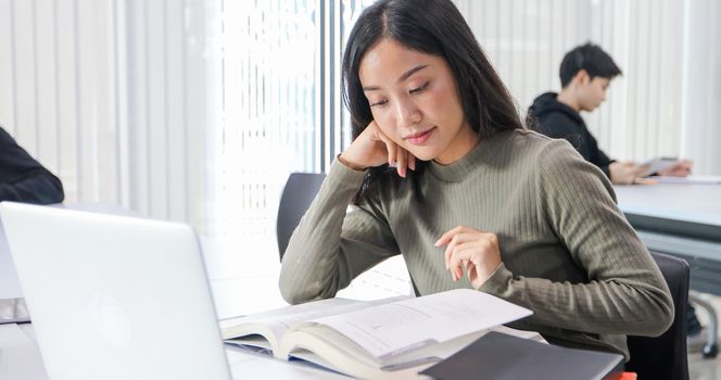 Asian women Students Smile and reading book and using notebook for helps to share ideas in the work and project. And also review the book before the exam
