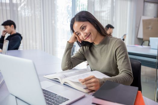 Asian women Students Smile and reading book and using notebook for helps to share ideas in the work and project. And also review the book before the exam