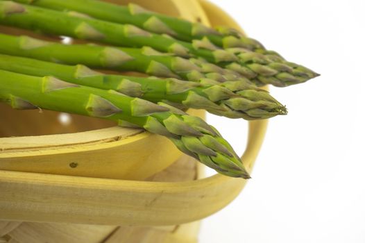 Bundle of fresh green asparagus in a rustic woven basket isolated on white background, selective focus