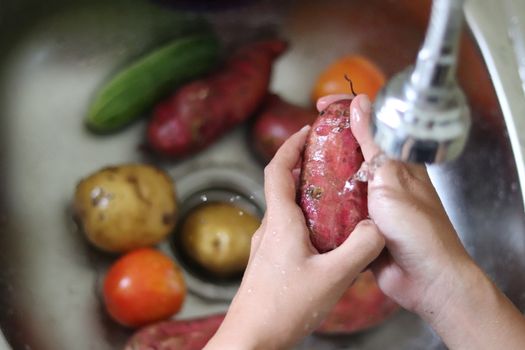 Top view of a woman's hands washing fresh vegetables in the kitchen sink