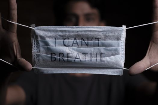 Young man holding medical mask with I Can't Breathe inscription on it. Cooncept of Protest about racial discrimination of Black People in U.S. America