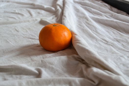 An orange fruit on an unmade bed showing concept of healthy lifestyle, home life and stay at home order during the covid-19 pandemic