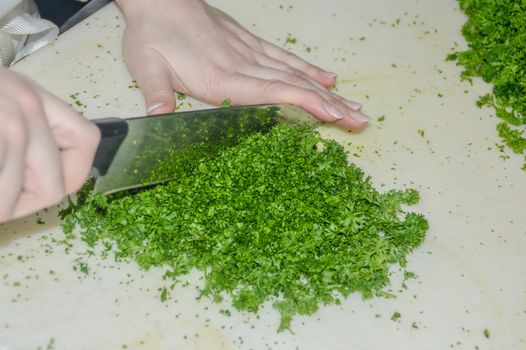 A kitchen worker chopping fresh parsley for cooking at a restaurant kitchen