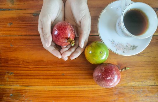 Flat layout photo of a hand holding a passion fruit beside a cup of black coffee, shows the concept of veganism, environmentalism and sustainable lifestyle