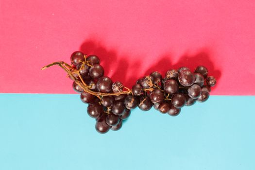 Red grapes against vibrantly colored pink and blue background to depic summer