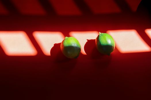 Two green limes against a red background with shadow lines that shows the concept of health and wellness