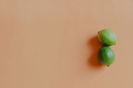 Two green limes against a soft pastel colored background showing the concept of health and wellness