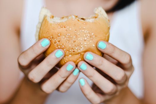 Close up of a hand with blue colored nail holding a half-eaten burger