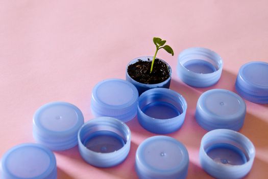 Seedling growing out among plastic bottle caps that shows the concept of hope for nature and the fight against plastic pollution