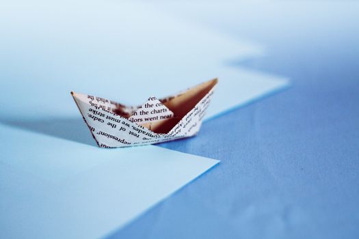 A paper boat made from old newspaper page against blue colored paper showing the concept of childhood dream, aspirations, hope and finances