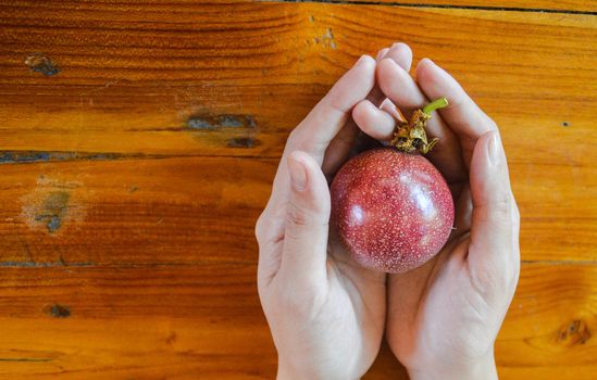 top view of a hand holding a passion fruit against wooden table