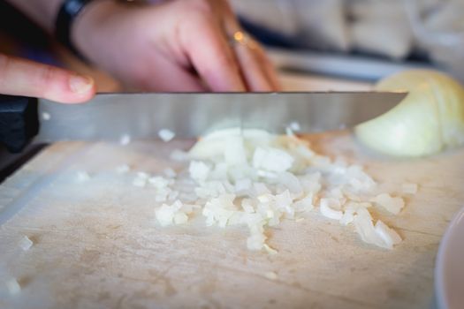 woman cuts onions on a white plastic board in a kitchen