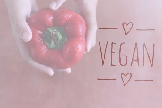 Hand holding a red bell pepper with Vegan text overlay