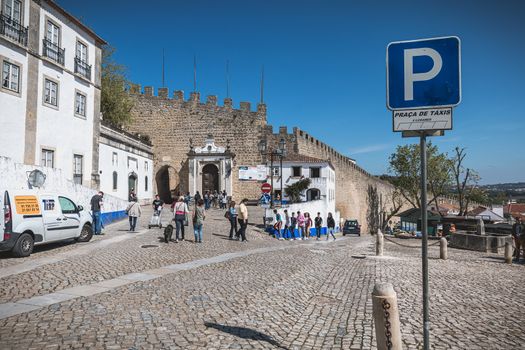 Obidos, Portugal - April 12, 2019: Tourists walking towards the entrance gate of the historic city on a spring day