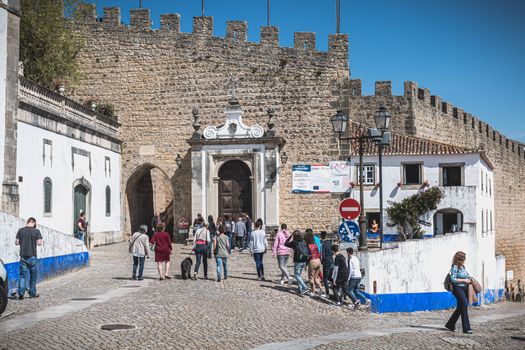 Obidos, Portugal - April 12, 2019: Tourists walking towards the entrance gate of the historic city on a spring day