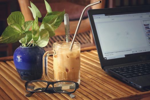 A laptop with iced coffee and reading glasses showing the concept of living the new normal by working from home to fight the spread of covid-19 pandemic