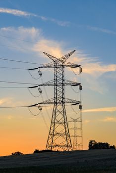 Electricity pylons and high voltage power lines at sunset