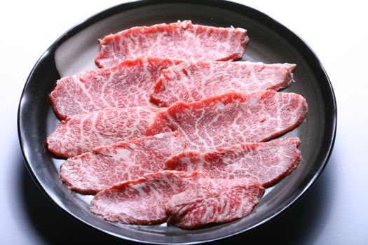 Raw Kobe wagyu beef sliced on black plate, white background