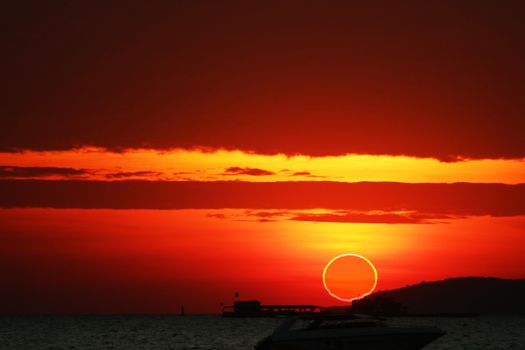 amazing phenomenon of partial sun eclipse over silhouette boat on sea and sunset sky