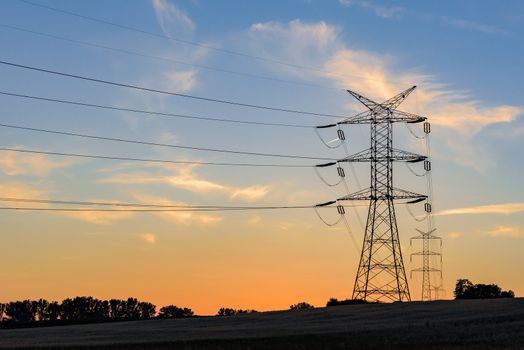 Electricity pylons and high voltage power lines at sunset