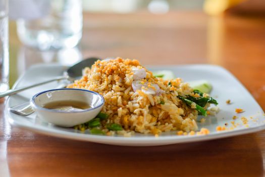 Delicious Thai food. Fried rice with egg, Kale served with minced red and green chilli in white plate on wooden table in cafe and restaurant. Selective focus.