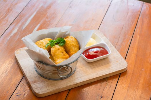 Delicious deep fried chicken nuggets on white paper in metal bucket on wooden tray and rustic table with blurry ketchup and mayonnaise. Unhealthy food concept.