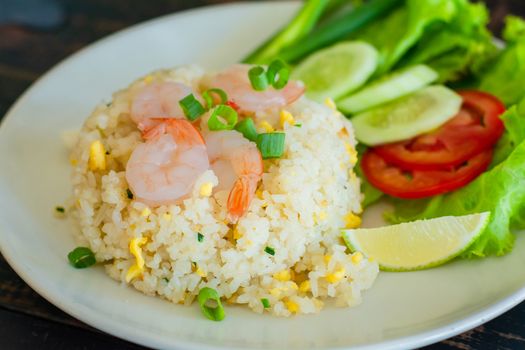 Close up fried rice with shrimp, egg and green onion on white plate serve with blurry cucumber, red tomato, lettuce in cafe and restaurant.