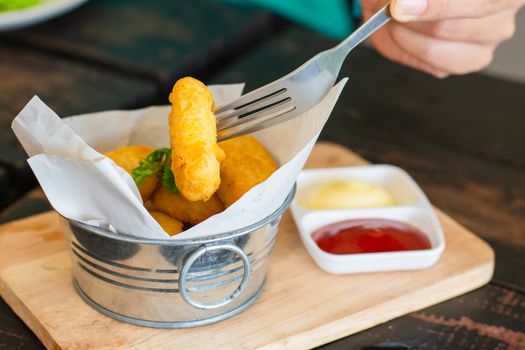 Delicious deep fried chicken nuggets on white paper in metal bucket on wooden tray and rustic table with blurry ketchup and mayonnaise. Unhealthy food concept. Eatting with fork.