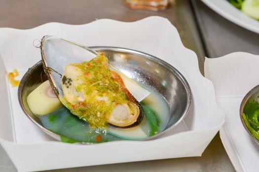 Steamed mussels with seafood sauce and Thai herb (sliced lemongrass) in metal bowl on white paper plate in chinese restaurant.