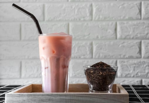 A glass of iced rose tea latte with dried tea leaf.