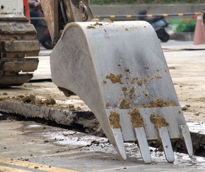 The digging bucket of a backhoe next to a ditch