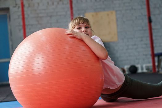 girl 8 years old with blond hair plays with a fitball in the gym