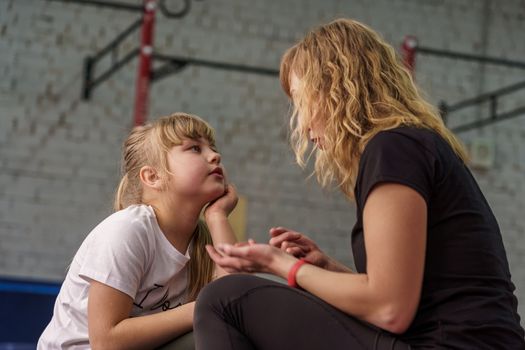 30 years old woman with blond hair talks to her daughter before training in the gym