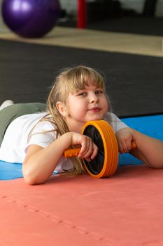 girl 8 years old with blond hair trains in the gym with a roller for the press