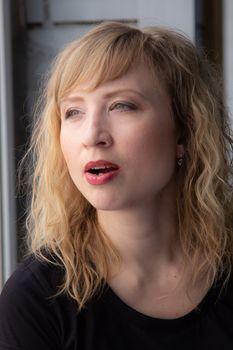 A woman of 30 years with blond hair near the window, you can see her reflection. Close-up