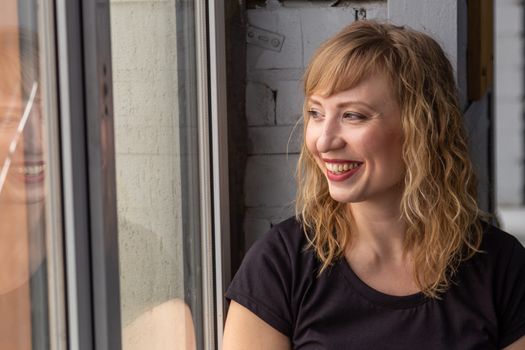 A woman of 30 years with blond hair near the window, you can see her reflection. Close-up