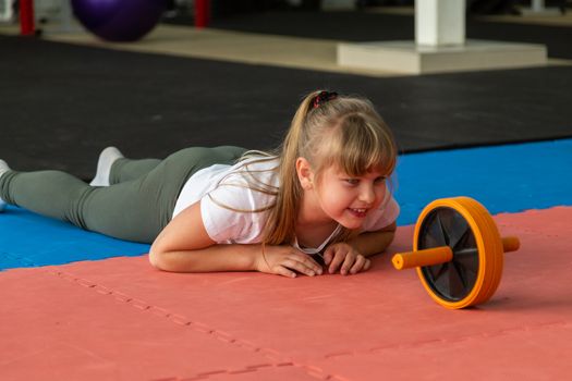 girl 8 years old with blond hair trains in the gym with a roller for the press