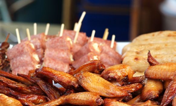 Barbecued chicken wings and ham skewers for sale at an outdoor stall
