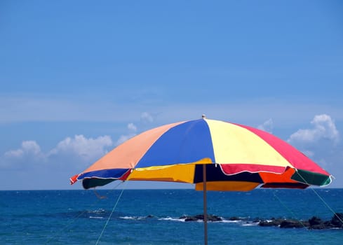 A colorful beach umbrella with a blue ocean in the background