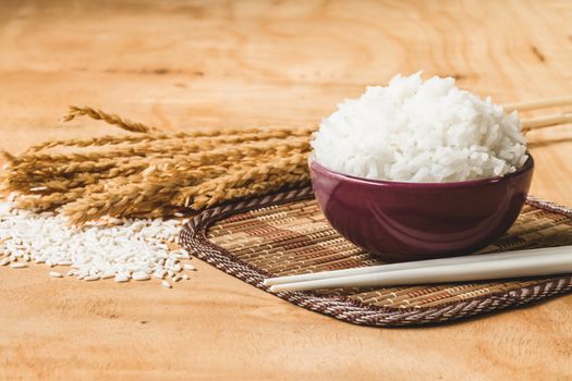 Cooked rice in bowl with raw rice grain and dry rice plant on  wooden table background.