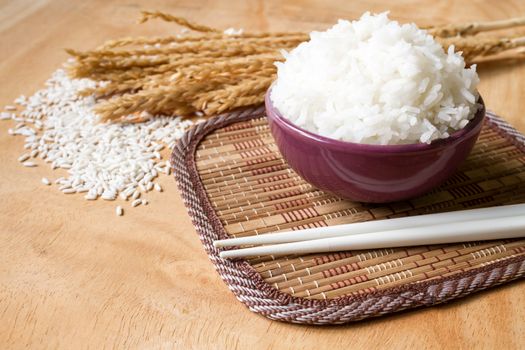 Cooked rice in bowl with raw rice grain and dry rice plant on  wooden table background.