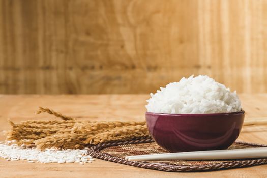 Cooked rice in bowl with raw rice grain and dry rice plant on  wooden table background.