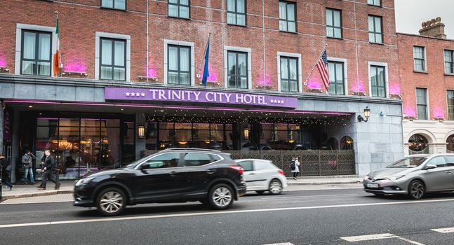 Dublin, Ireland - February 11, 2019: People and cars driving past the facade of the luxurious Trinity City Hotel in the city center on a winter day