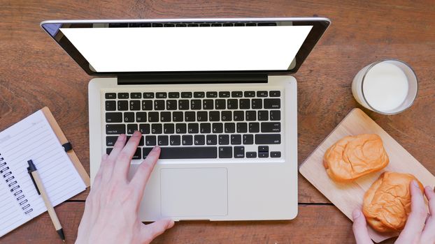 Labtop,notebook,bread and cup of milk with hands on wooden table background.