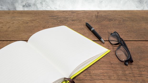 Blank notebook with pen and glasses on wooden table.